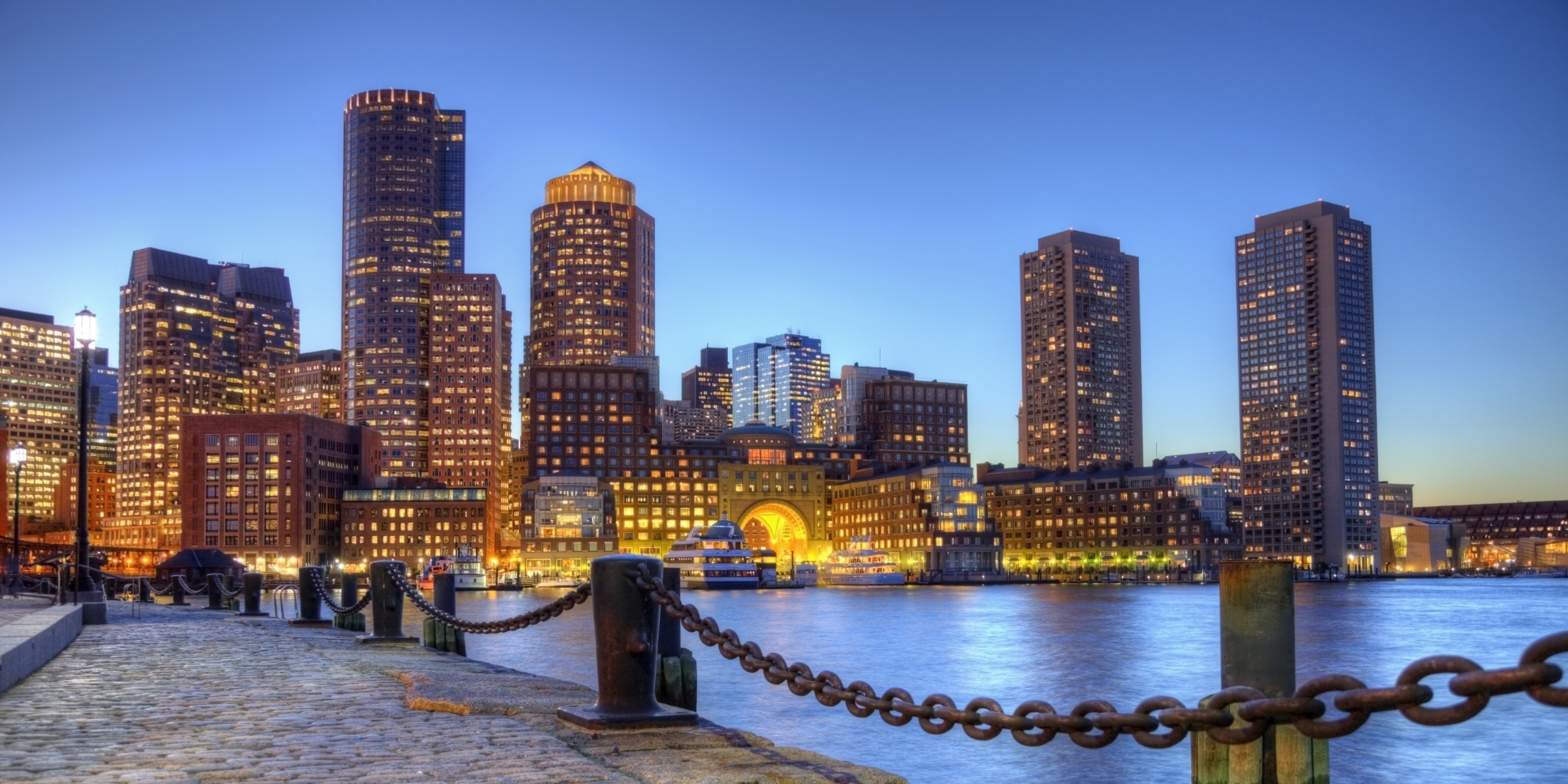 Photo taken along the waterfront at night in the South Boston southie neighborhood at night. The Boston cityscape is a mixture of old and new buildings. Boston is the capital and largest city in Masssachusetts. Boston is the largest city in New England